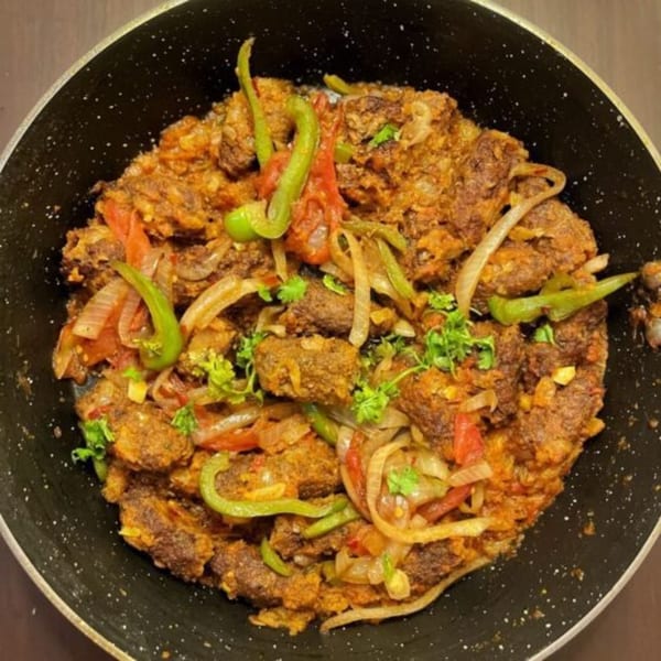 Nosh Kabob's Pakistani dish with meat, onions, tomatoes, green peppers, and cilantro in a black pan.