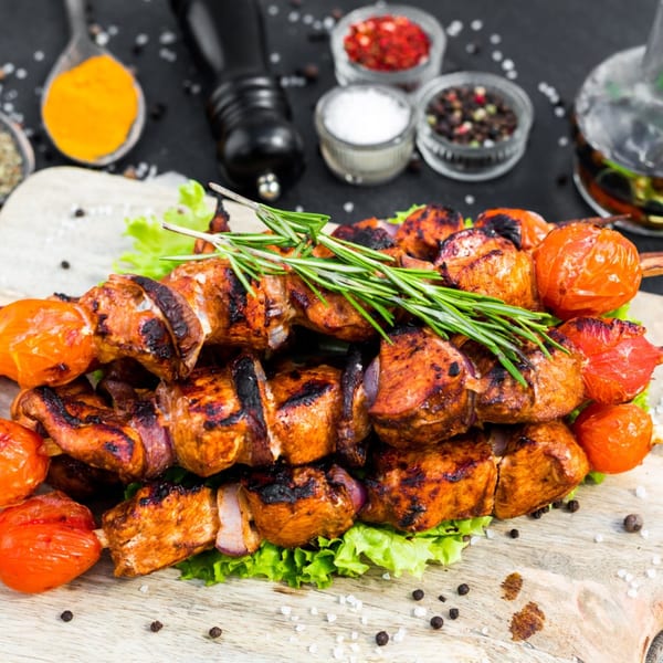 Grilled chicken and tomato Pakistani kabobs on a bed of lettuce with spices in the background.