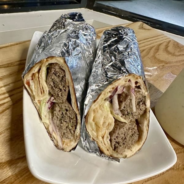 Two Nosh Kabob wraps, partially unwrapped from foil, revealing meat and fillings on a white plate.