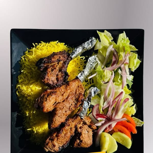 Nosh Kabob's Pakistani lamb chops with yellow rice and a fresh salad on a black plate.