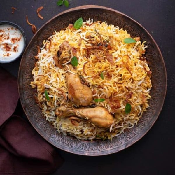Chicken Biryani with two drumsticks, rice, fried onions, and mint, served with raita.