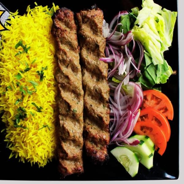 Two Nosh Kabob seekh kebabs with yellow rice, sliced red onions, lettuce, tomatoes, and cucumbers.